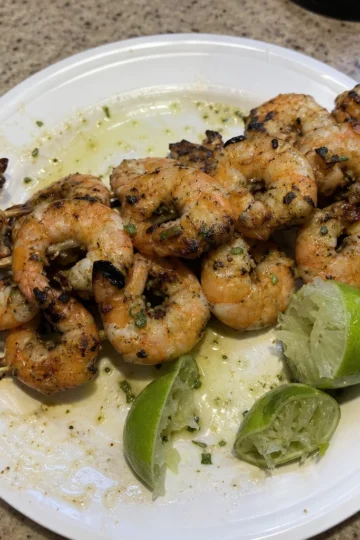 Grilled shrimp skewers on a barbecue grill with peppers and lime wedges