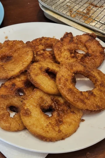Delicious fried cinnamon apple rings on a plate, dusted with powdered sugar.