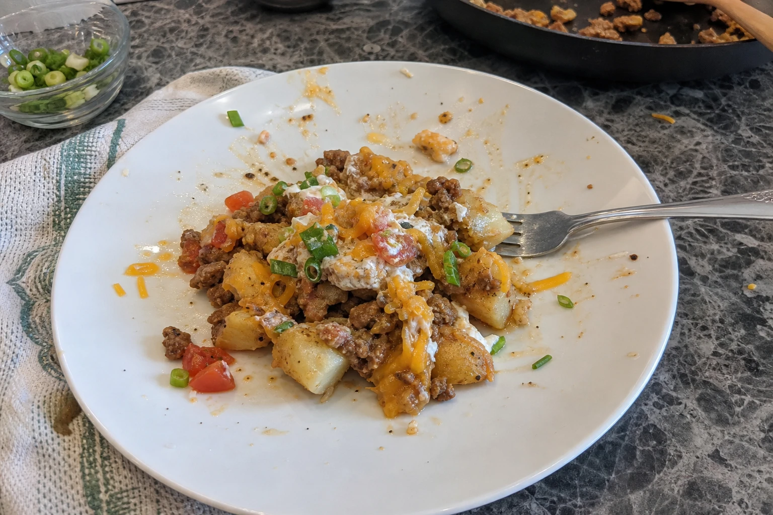 Close-up of crispy roasted potatoes in a taco bowl topped with shredded cheese, sour cream, and fresh herbs, inviting you to indulge.
