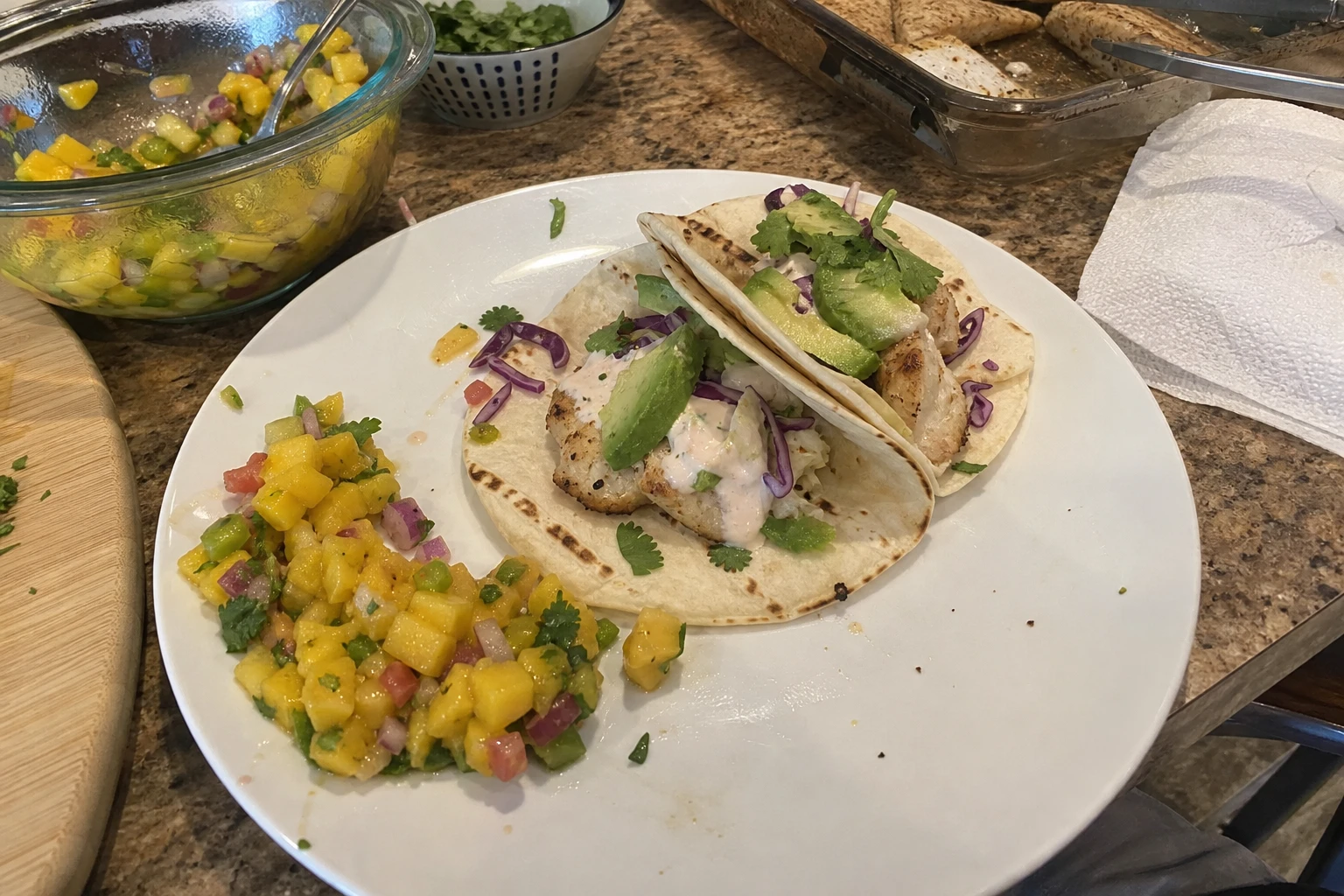 A plate of fish tacos with fresh avocado and lime wedges