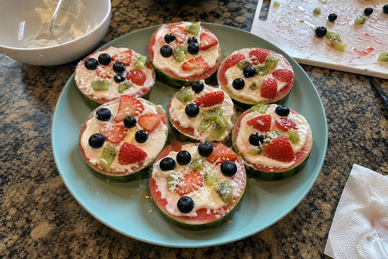 A hand reaching for a slice of watermelon pizza topped with berries and yogurt.