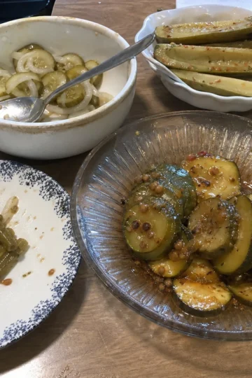 Homemade dill pickles in a jar with fresh herbs and spices nearby.