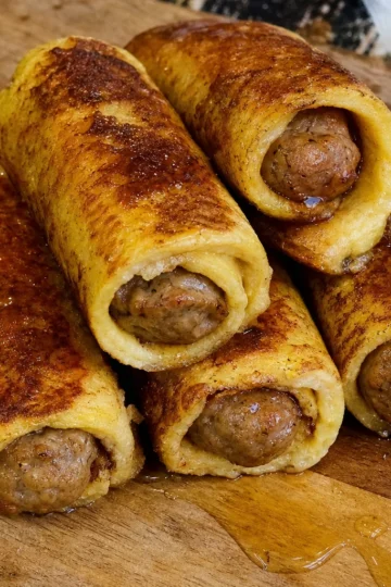 Deliciously golden Sausage French Toast Roll-ups plated with powdered sugar and maple syrup.