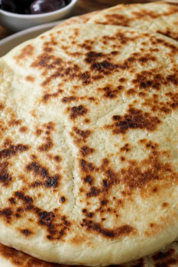 A golden-brown bazlama bread on a rustic wooden board