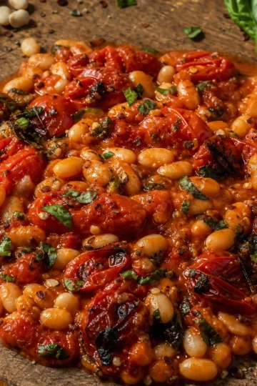 A bowl of creamy white bean and roasted tomato stew garnished with fresh basil.